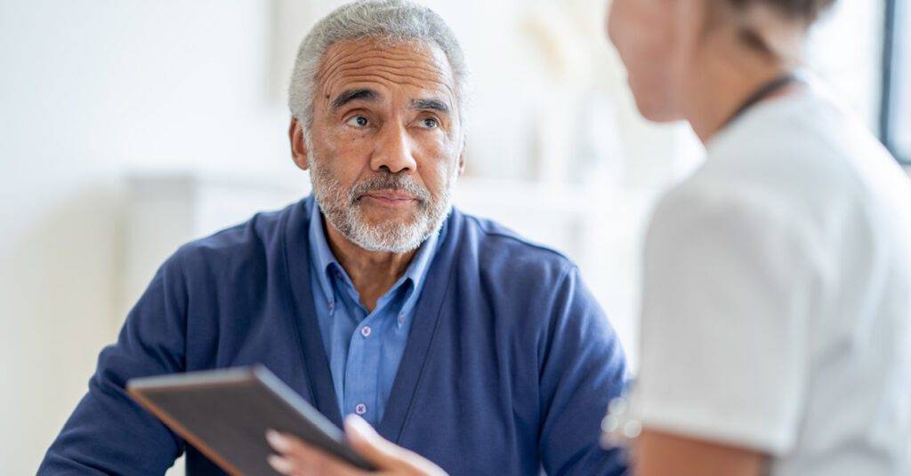 elderly man talks to healthcare professional with ipad